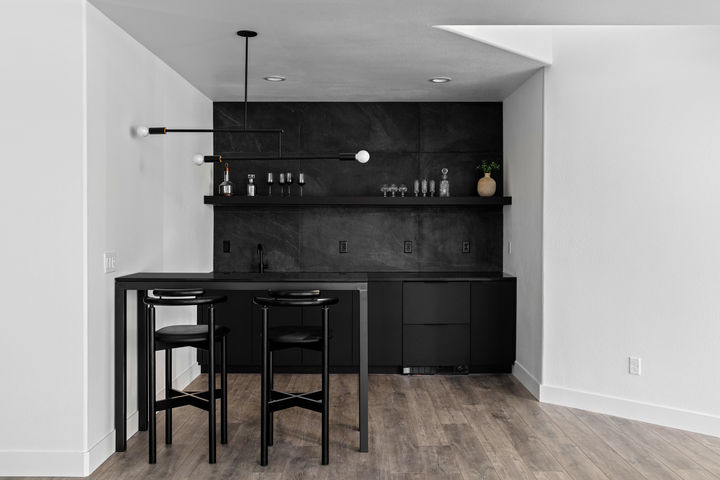 Modern black kitchen bar with open wooden shelves, glassware, and a matte black faucet