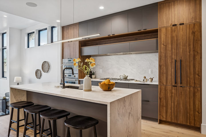 Modern kitchen featuring walnut cabinetry, charcoal cabinets, waterfall quartz island, and linear pendant lighting.