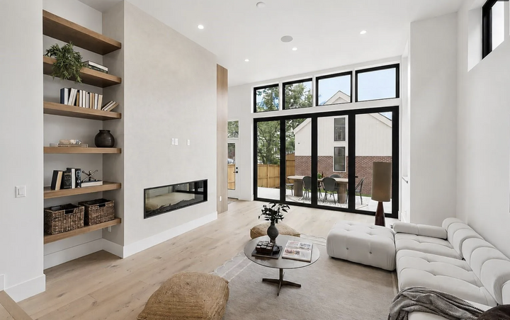 Modern great room with linear fireplace, floating wood shelves, contemporary sectional sofa, and large sliding glass doors.
