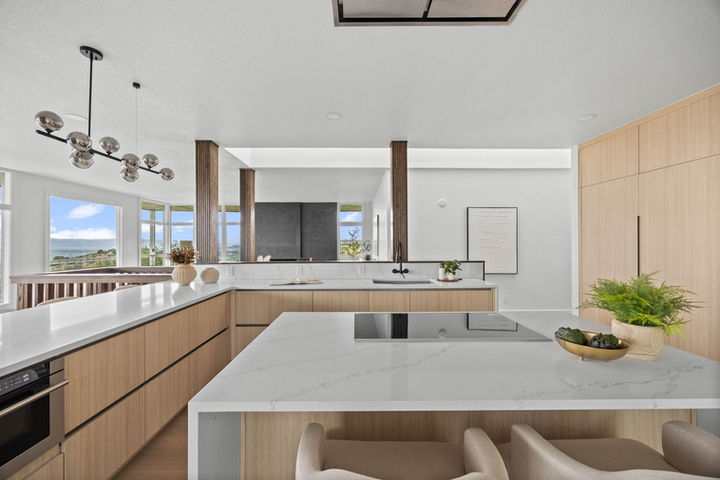 Modern open kitchen with large quartz waterfall island, natural wood cabinetry, black fixtures, and mountain views through expansive windows. Faver Drive Remodel
