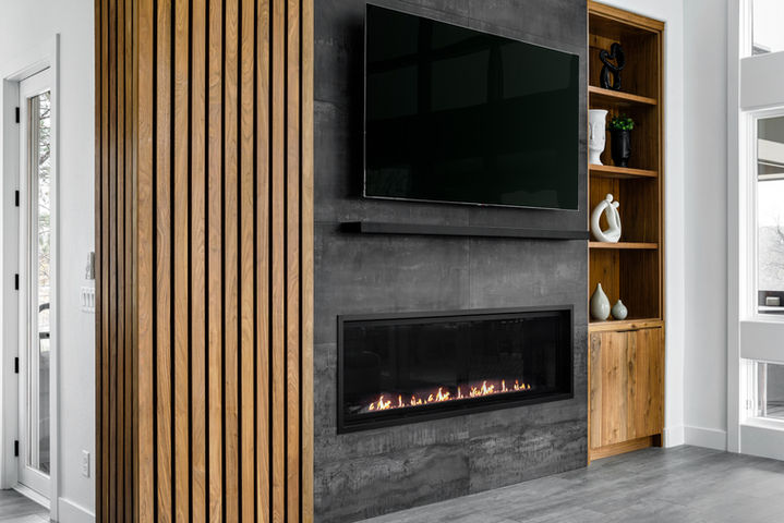 Modern family room fireplace with charcoal tile, linear gas fireplace, wall-mounted TV, walnut slatted column, and open wood shelving with sculptural decor.