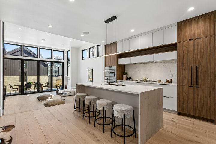 Luxury modern kitchen with walnut and white cabinetry, waterfall marble island, and open-concept living room in a Denver LoHi residence.