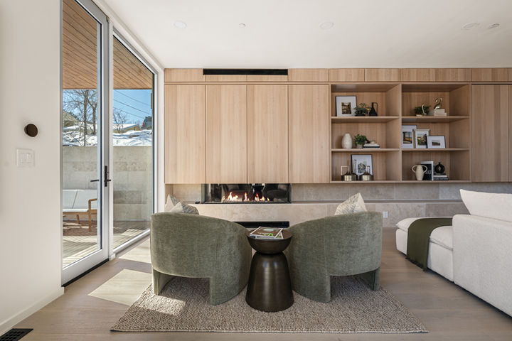 Living area with green accent chairs in front of a fireplace, framed by tall sliding glass doors – Boulder luxury home.