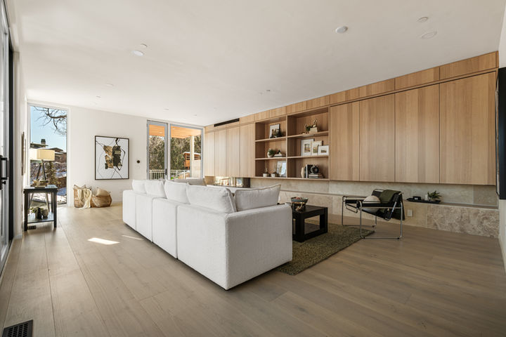 Wide view of Alpine Drive living room showcasing dual seating, custom cabinetry, and wet bar connection to kitchen.
