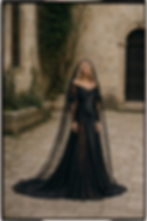 Bride in a black satin gown with black lace sleeves and side panels, a rosette waist detail, and a lace-edged black veil in a stone courtyard. Studio RÉN.
