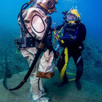 Old style dive equipment vs new style dive equipment. Man with kirby morgan helment on is using up to date outland dive light and dive camera