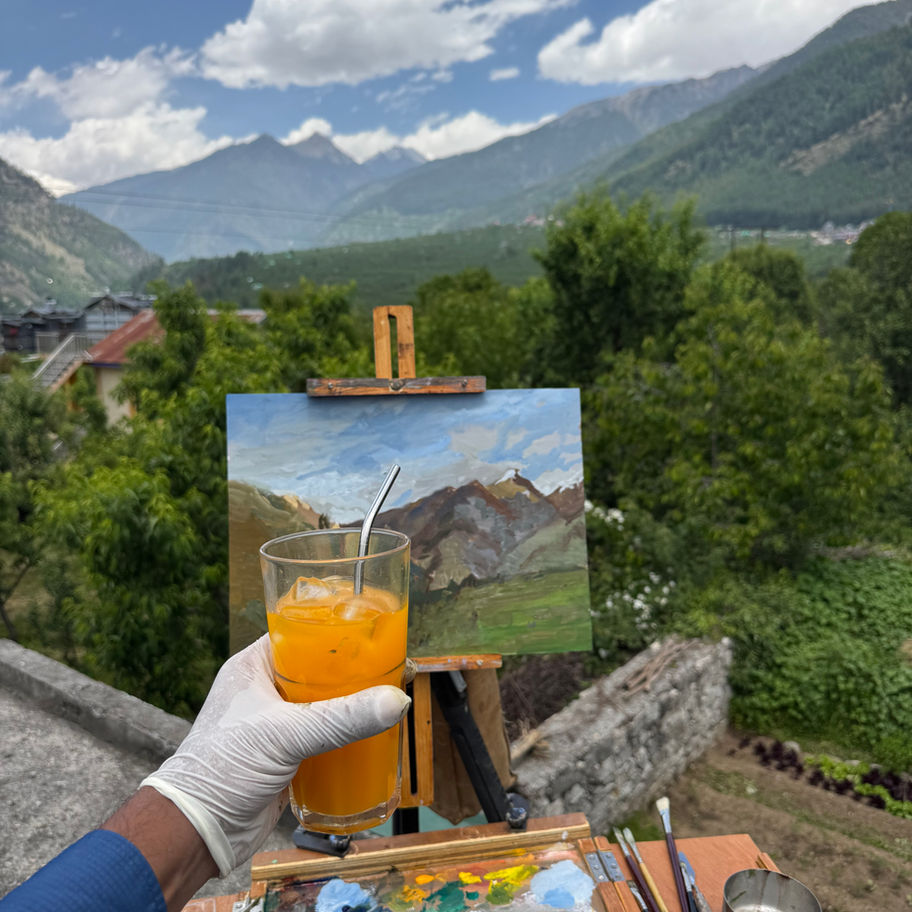 Artist painting mountainscape outdoors with orange drink