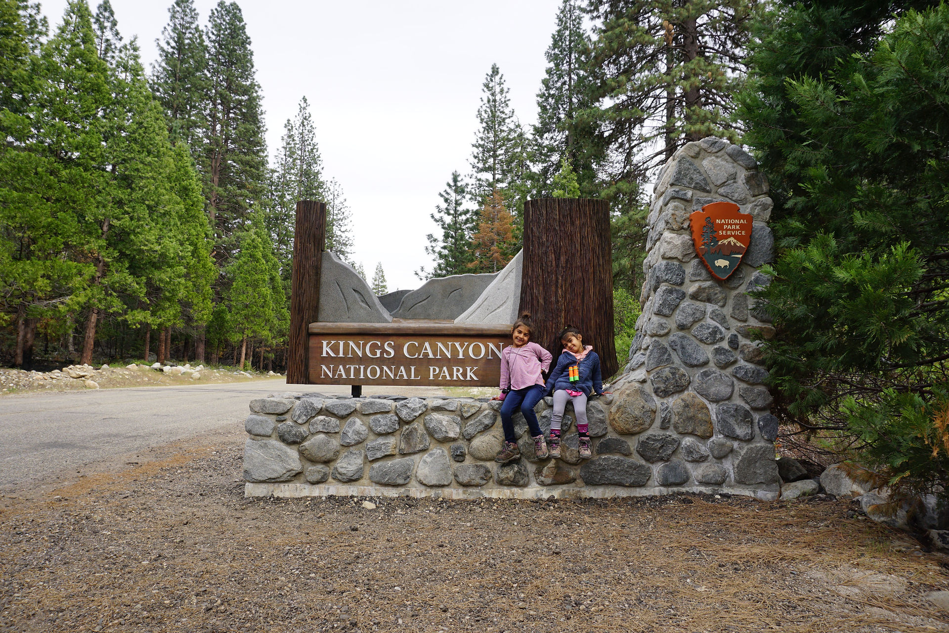 Family standing at the Kings Canyon National Park entrance sign in the Giant Sequoia forest