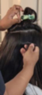 Licensed hairstylist professionally installing invisible tape-in hair extensions using premium Asian human hair for a seamless, natural-looking result.