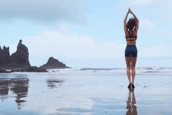 Frau im Bikini macht Jumping Jacks am Strand. MorningFit.org