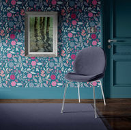 Vector illustration of stylised leaves and flowers in multiple bright colours pink, mauve, in a repeat pattern on a teal blue background shown on a wallpaper in an interior scene