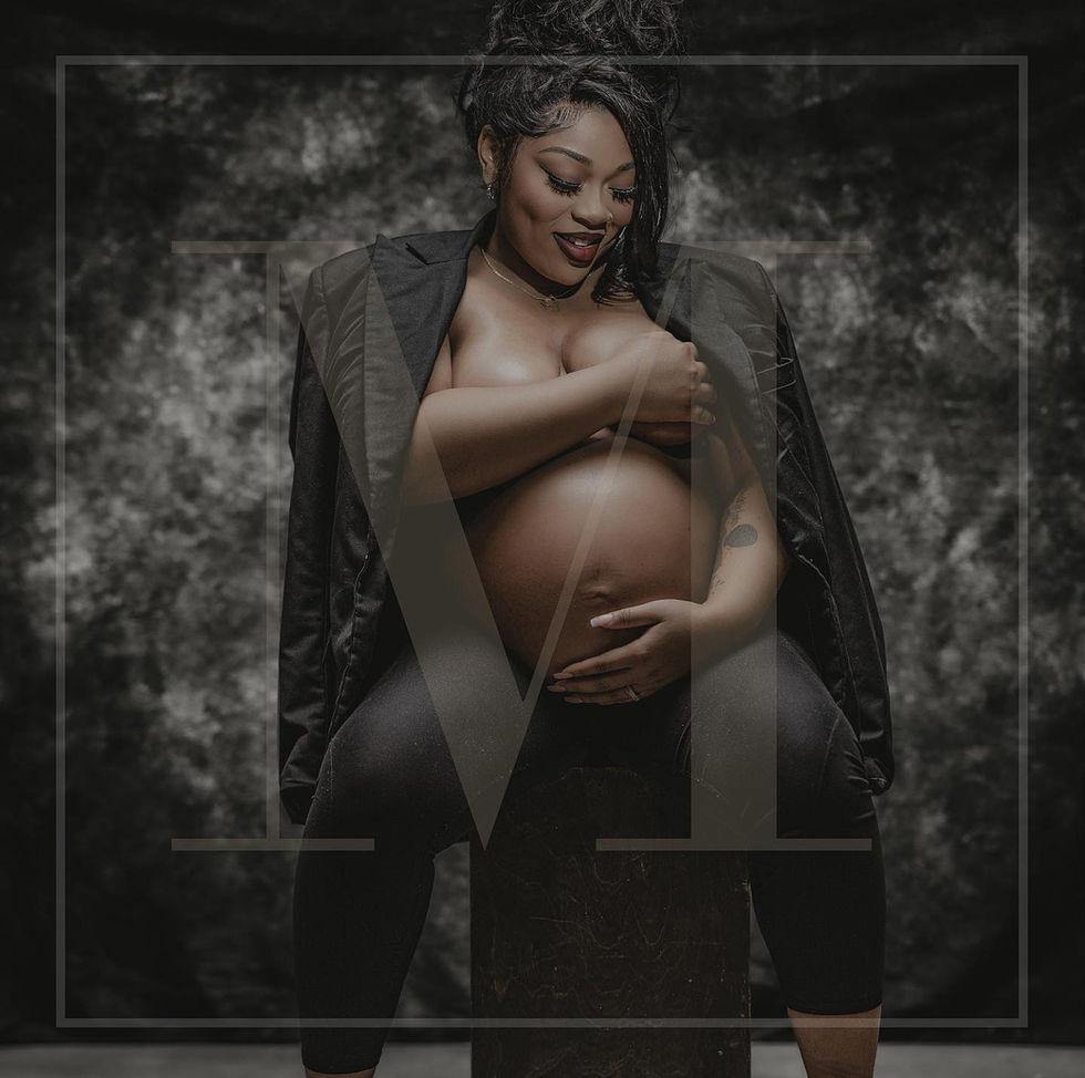 Pregnant Black woman in a black blazer smiling and holding her belly in a dramatic, softly lit maternity portrait by Shooters Society Studios.