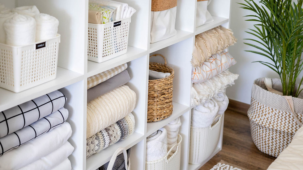 Neatly folded towels and linens in white shelves, with woven baskets and a potted plant. Bright, organized, and tidy atmosphere.