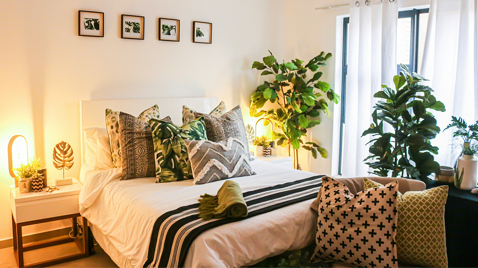 Bedroom with a neatly made bed featuring patterned pillows and a striped throw. Green plants decorate the room, creating a cozy, vibrant mood.