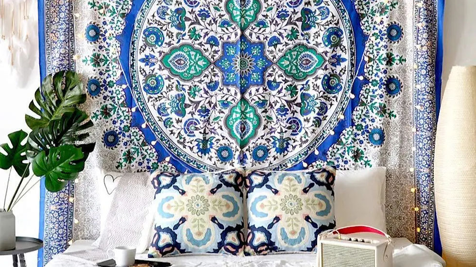 Bohemian-themed room with a blue and green mandala tapestry, patterned cushions on a bed, a tall lamp, tropical plant, and a radio.