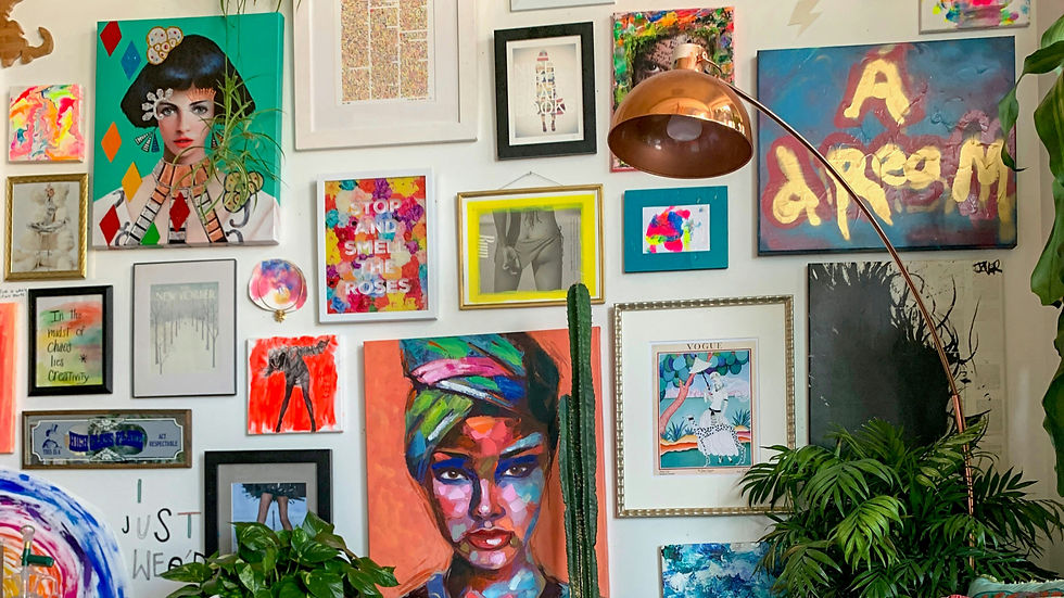 Colorful wall gallery with mixed art and photos, including portraits and abstract pieces. A copper lamp and green plants add vibrancy.