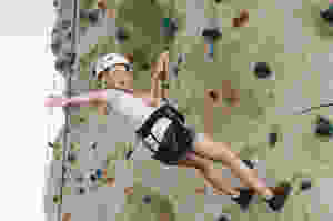 Young girl smiling and waving while rock climbing for the first time on an indoor rock climbing az gym