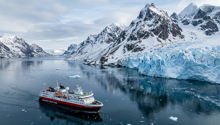 Wide-angle view of an expedition ship sailing beside snowy Svalbard mountains