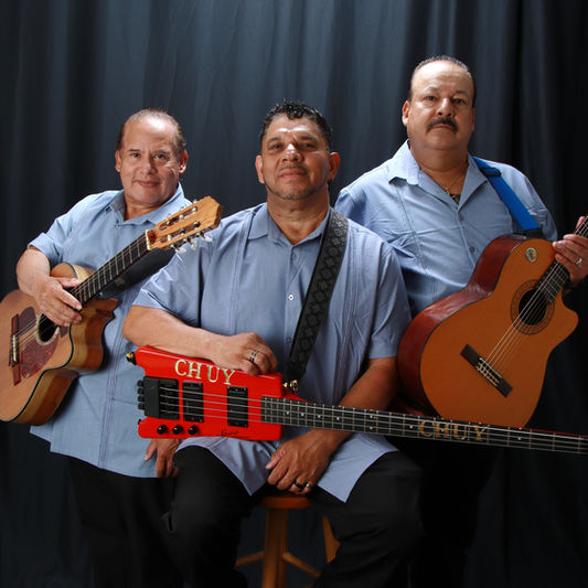 Trio of mariachis in blue shirts holding guitars and posing professionally.