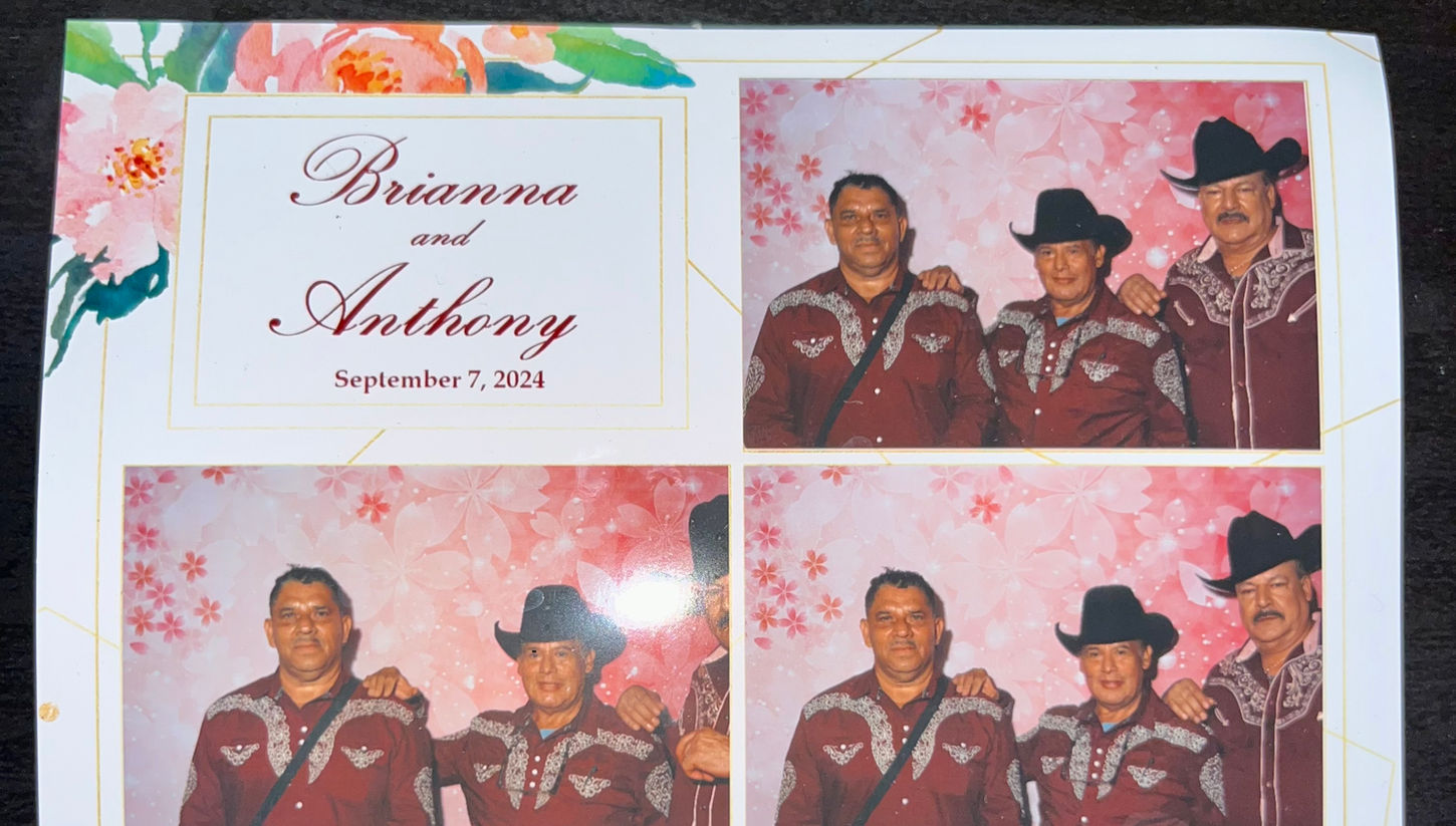 Three members of Trio Mariachi Tepatitlán dressed in maroon traditional outfits, posing for photos at Brianna and Anthony's wedding on September 7, 2024, in front of a pink floral backdrop.