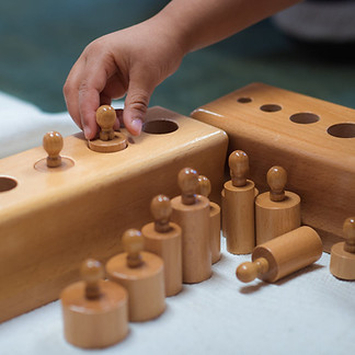 A child's hand puting a wooden chip on a wooden box with some holes.