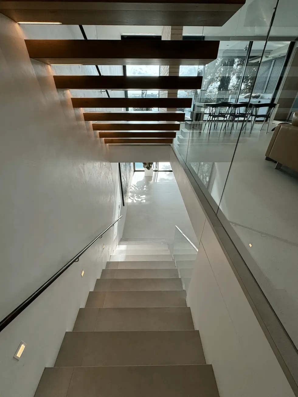 Modern staircase with wooden steps, white walls, and glass railing.