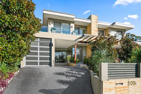 Modern two-story home with a balcony, landscaped yard, and a paved driveway.