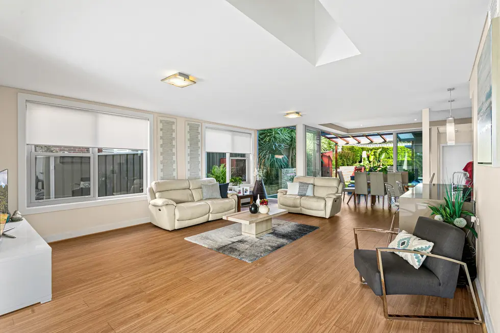 A spacious living room with comfortable furniture and large windows. The open-plan design connects to the dining area and kitchen.