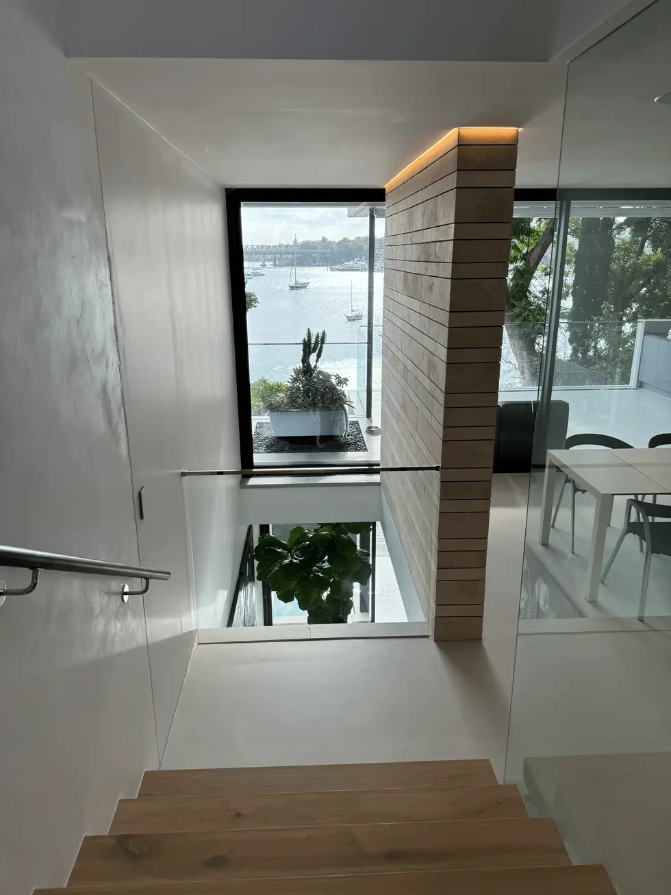Modern staircase with glass railing leading down to a garden with a water view.