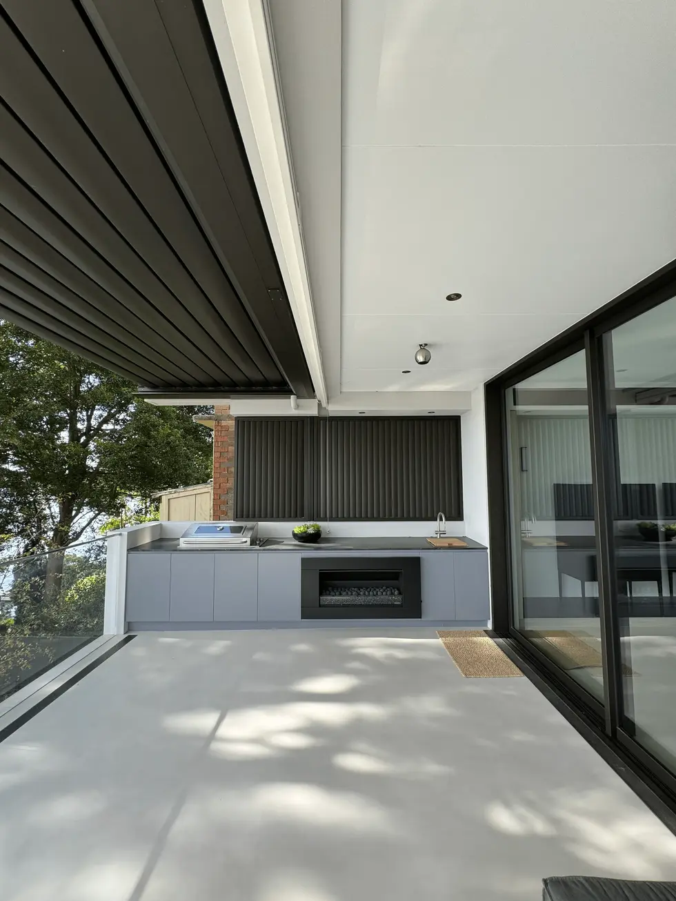 Modern outdoor patio with covered area, barbecue, fireplace, and sliding glass doors.