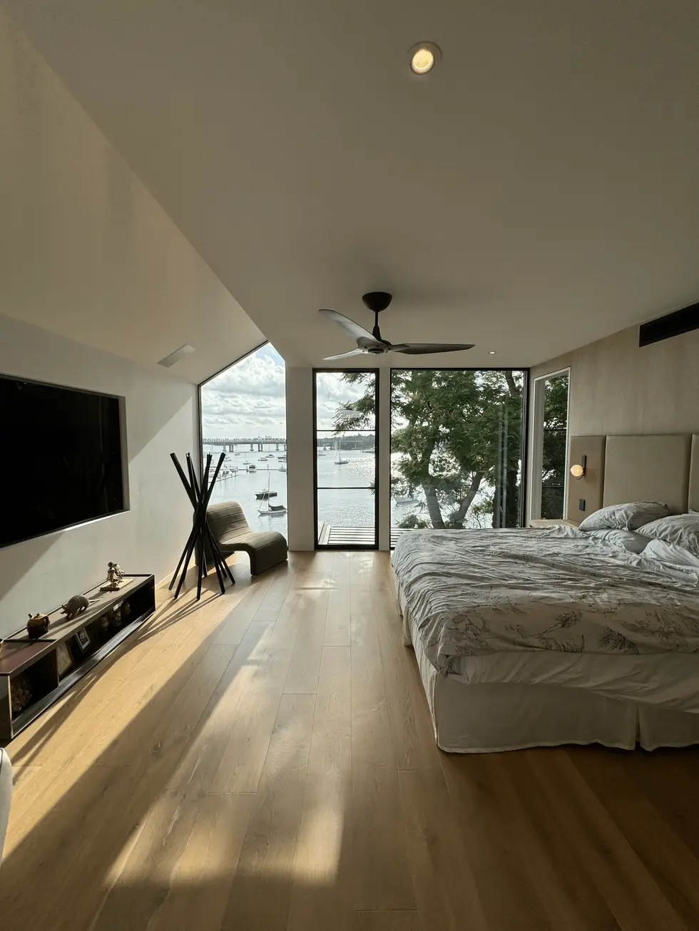 Modern bedroom with king-size bed, large window with water view, ceiling fan, and balcony access.