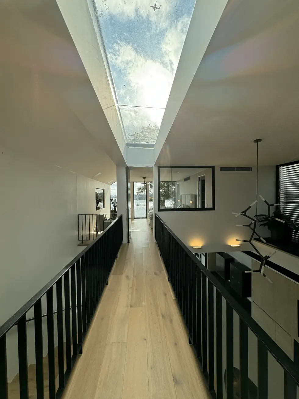 Modern hallway with skylight, wooden floors, and black metal railings.