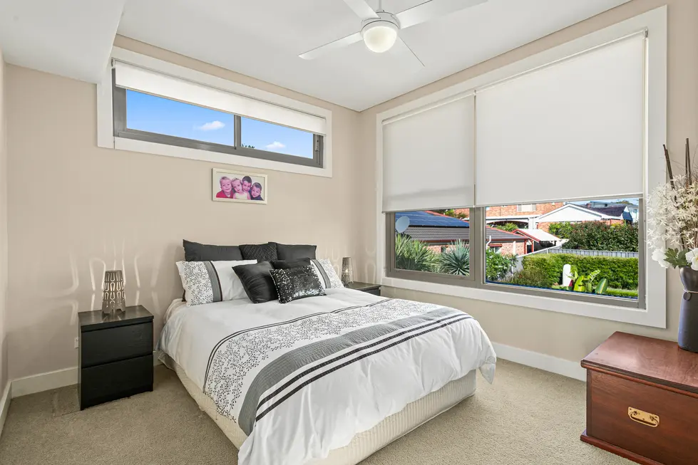 Bedroom with a bed, bedside tables, and windows overlooking a backyard.