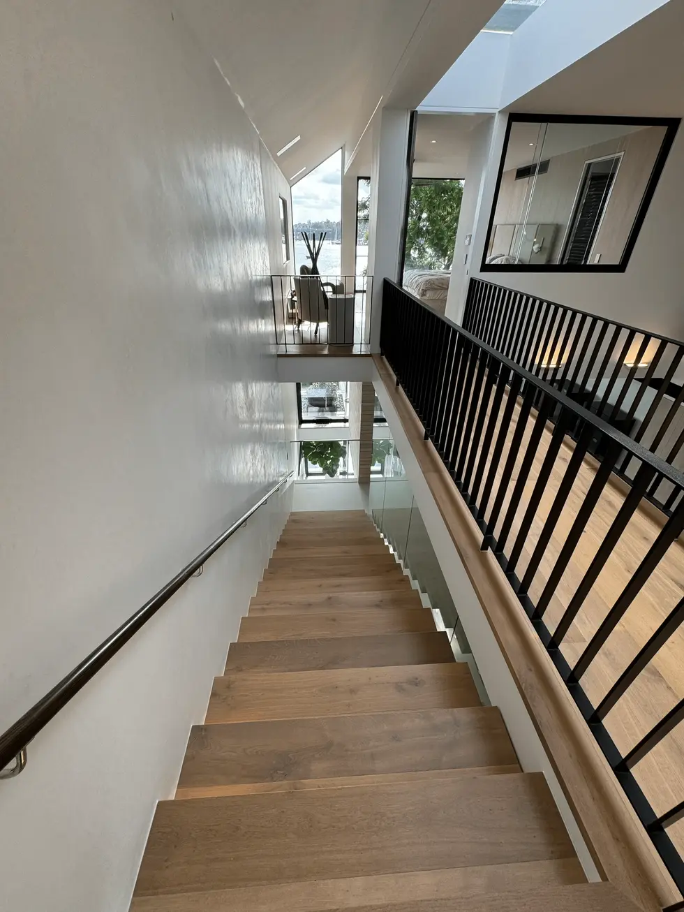 Modern staircase with wooden steps, white walls, and black metal railing.