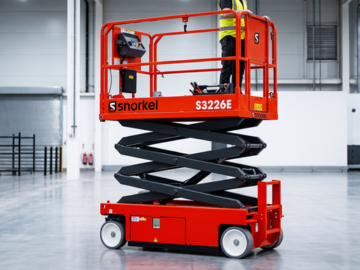 Persona de pie en plataforma elevadora roja Snorkel S3226E en un almacén amplio y vacío. Ambiente industrial y seguro.