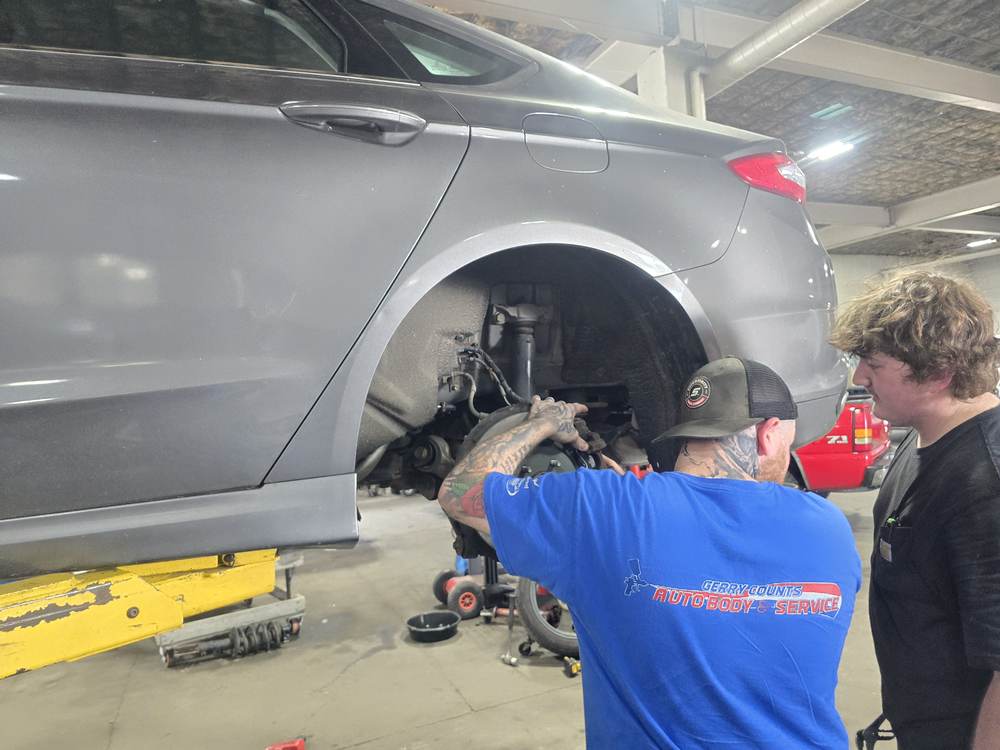 Technicians working on brakes at a vehicle's rear wheel on the service side
