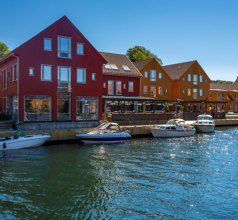 Fiskebrygga harbor in Kristiansand, Norway, with colorful buildings and boats reflecting on the water.
