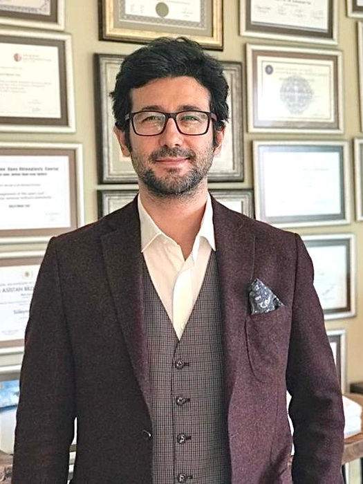 Professional office portrait of Prof. Dr. Suleyman Tas with academic certificates and medical achievements in the background.