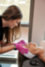 an aesthetician in pink gloves is working on a clients forehead
