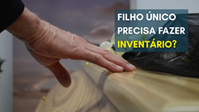 Mão repousando sobre caixão de madeira durante velório, simbolizando o luto de um filho único e a necessidade de realizar inventário após o falecimento dos pais.