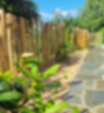 Jardin paysager avec un sentier en pierre naturelle, une clôture en bois et un ciel dégagé, conçu pour l'harmonie et la sérénité.