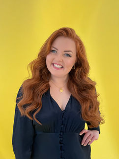 Lucy wearing a navy dress that is so dark it looks like it is black against a yellow background