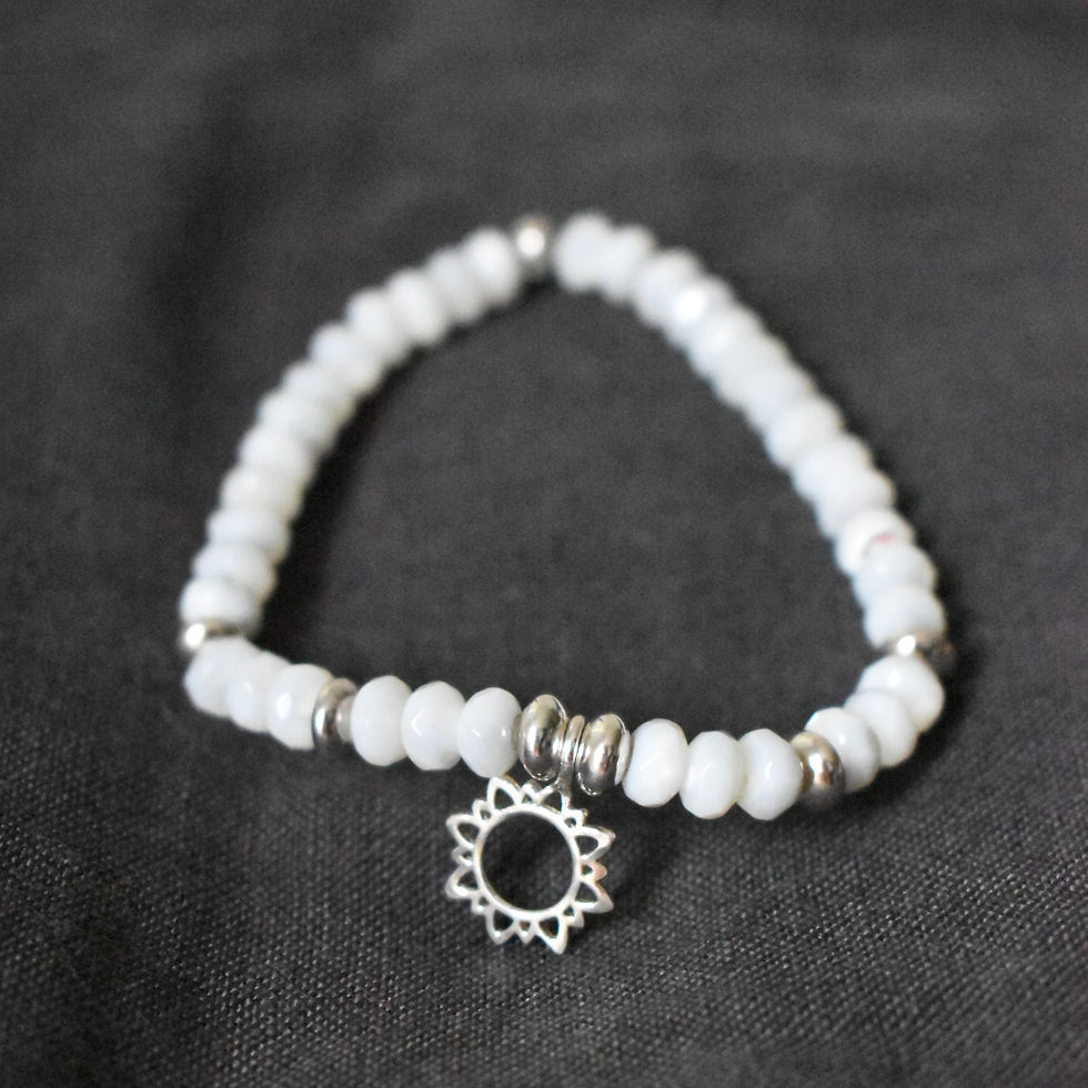 Armband aus facettierten Perlmutt Buttons mit silbrigem Sonne Anhänger vor dunklem Hintergrund