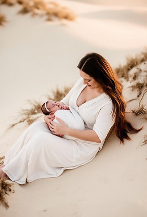 Pregnant woman in a flowing white dress holding her baby bump during an outdoor maternity photoshoot