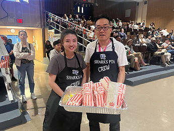 Two parents handing out popcorn at an IS 25 event in the auditorium