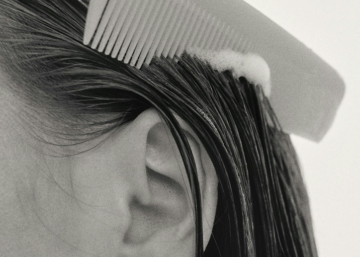 In a Japanese hair salon, a woman with long hair is combing her hair, with various salon tools visible around her.