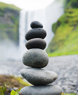 A small, vertical stacking of round rocks positioned in front of a waterfall in the background.