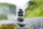 Stack of stones in focus with a blurred waterfall and greenery in the background.