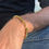 Thumbnail: Close-up of a man's arm wearing the Waterproof Gold Box Chain bracelet outdoors, showcasing the chunky square links in natura