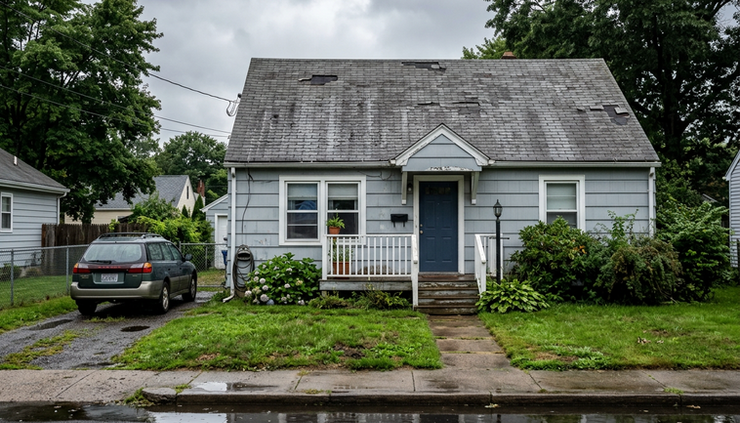 Wide-angle view of a single-family house with worn shingles after heavy rain